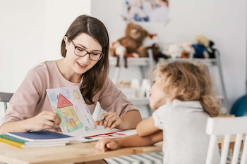 Woman and a young girl sitting at a table looking at the girl's drawing of a house