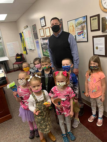 A man with a mask on behind children at school with masks on.