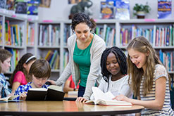 A group of children reading and a teacher overlooking them.