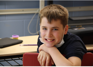Young boy smiling at a school desk with a mask on