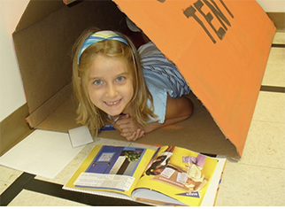 A kid laying in a play tent while reading a book.