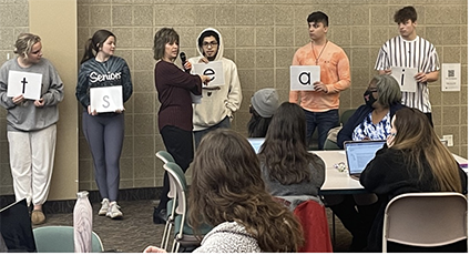 Students lined up in front of a crowd; each displaying a letter they are holding