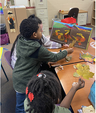 A student at school holding up a leaf and comparing it to a leaf in a book