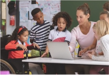 Elementary-aged children and teacher seated at a table looking at a laptop