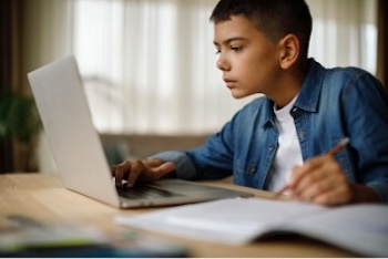 Middle school-aged boy at a laptop taking notes