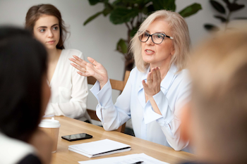 older woman in business attire speaking to colleagues at a table