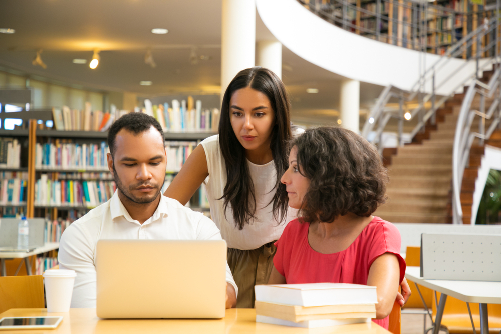 Three professionals around a laptop in a library