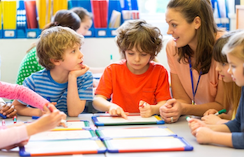 Two boys at a table in a classroom with their female teacher