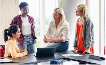 Woman teaching engaged young adults around a table with a laptop